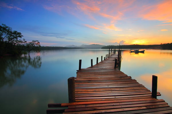 A picture of a dock stretching into a tranquil lake at sunset